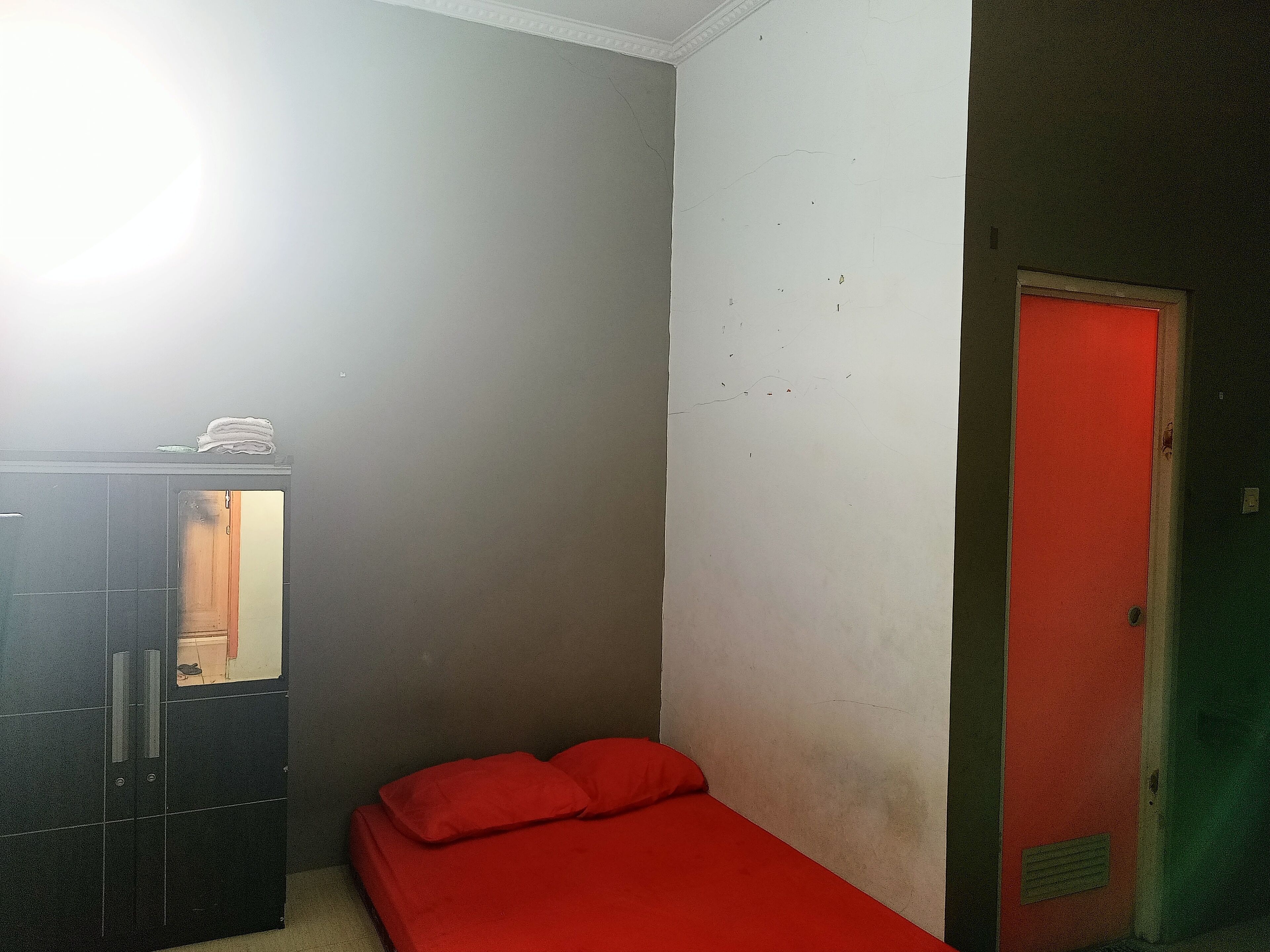 Ein kleiner, schwach beleuchteter Raum mit einem Bett, einem Kleiderschrank und einer roten Tür.