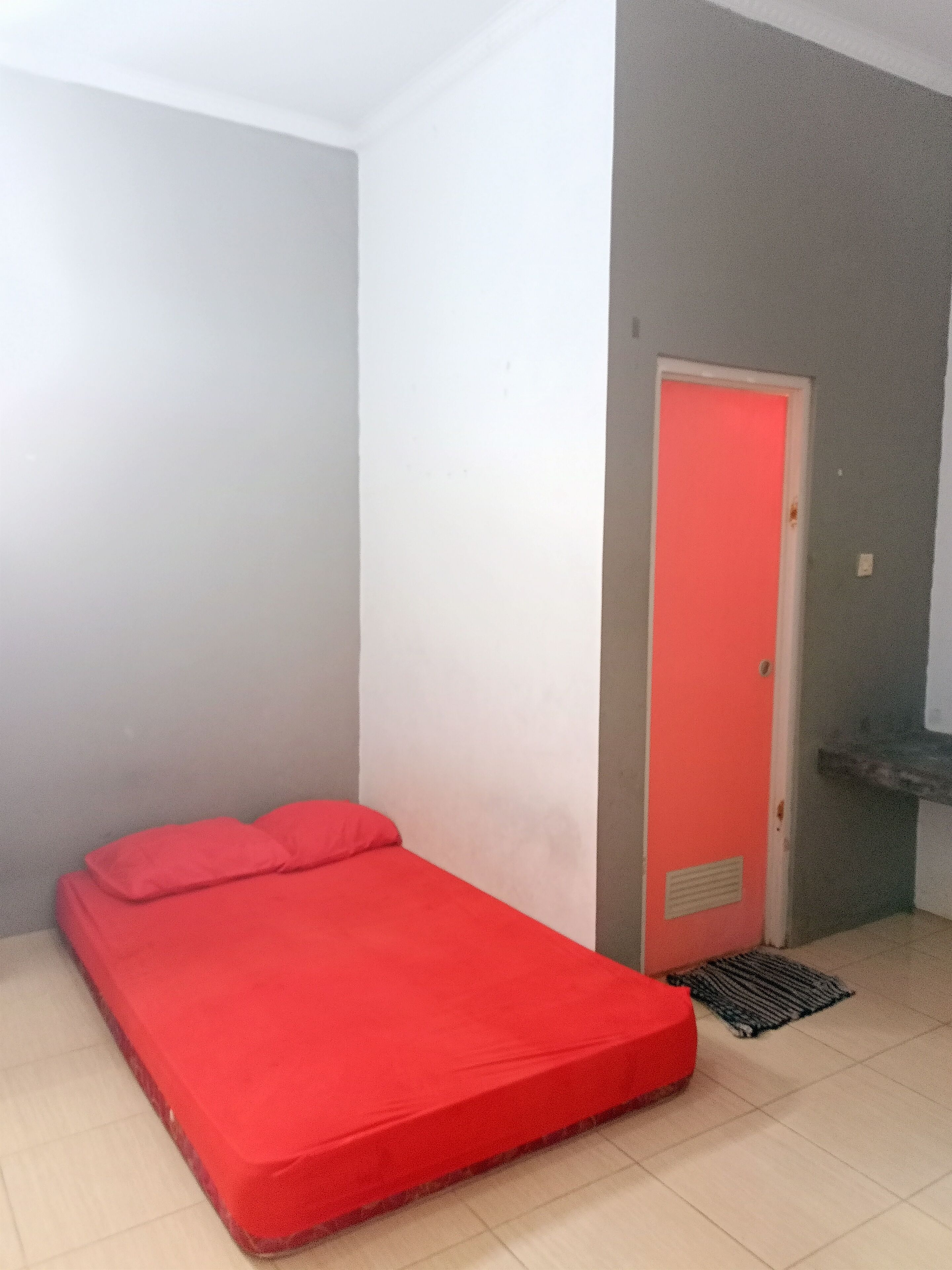Una habitación pequeña con una cama individual, una puerta y suelo de baldosas.