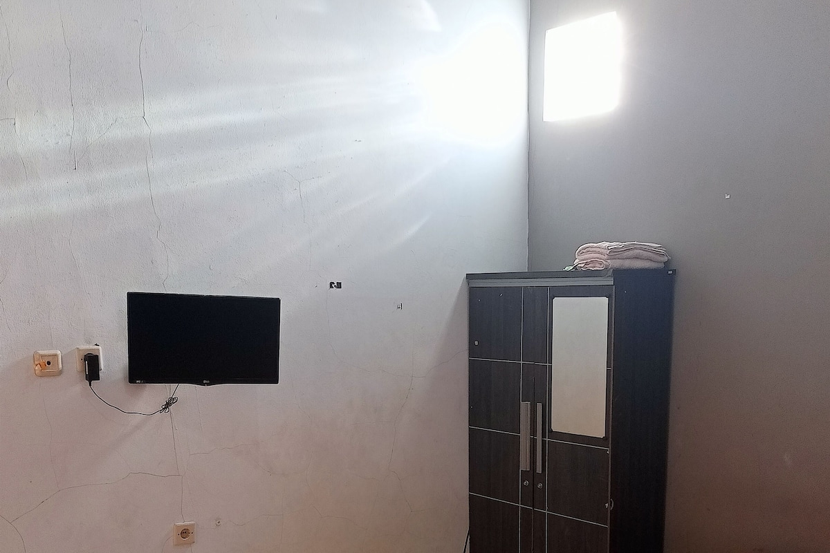 A room with a bed, a wardrobe, a wall-mounted TV, and a power outlet.