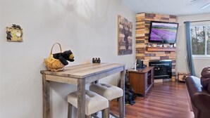 Una sala de estar acogedora con chimenea, un televisor montado en una pared de piedra, una mesa de comedor de madera y un sofá de cuero.
