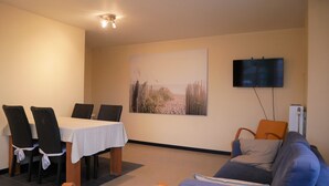 Un salon comprenant une table à manger, des chaises, un canapé, un téléviseur et un tableau accroché au mur.