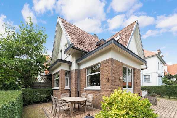 Een huis met een pannendak, bakstenen gevel en een terras met een tafel en stoelen.