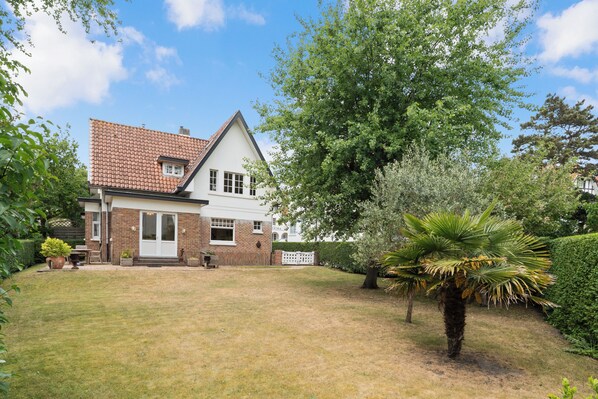 A two-story house with a tiled roof, a brick facade, and a well-maintained lawn. - Monina - 3 bedroom villa and a very spacious garden - 250 meters from the beach (De Haan)
