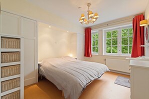 A bedroom with a bed, a window with red curtains, a radiator, and a chandelier. - Monina - 3 bedroom villa and a very spacious garden - 250 meters from the beach (De Haan)