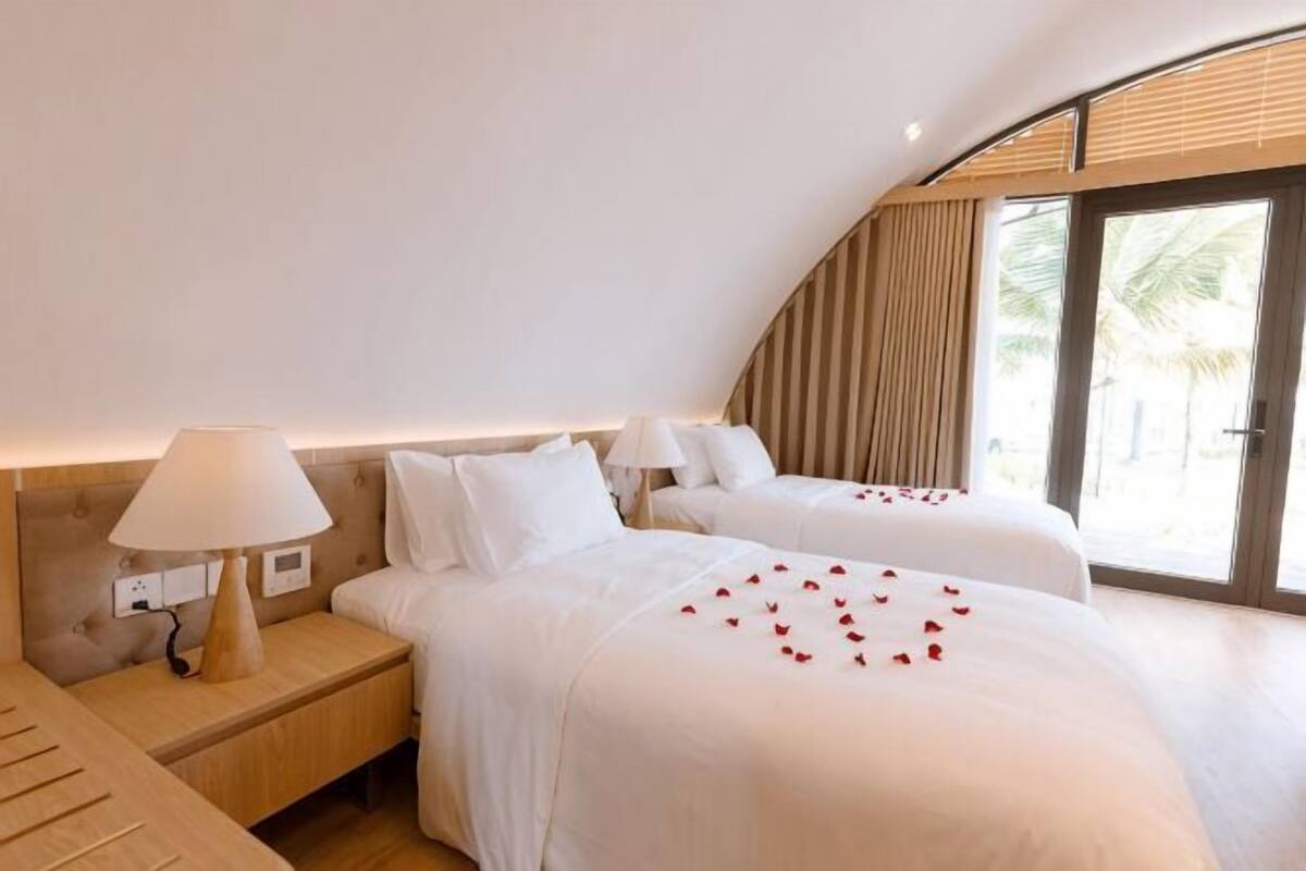 A hotel room with two beds, a nightstand, a lamp, and a large window with a view.