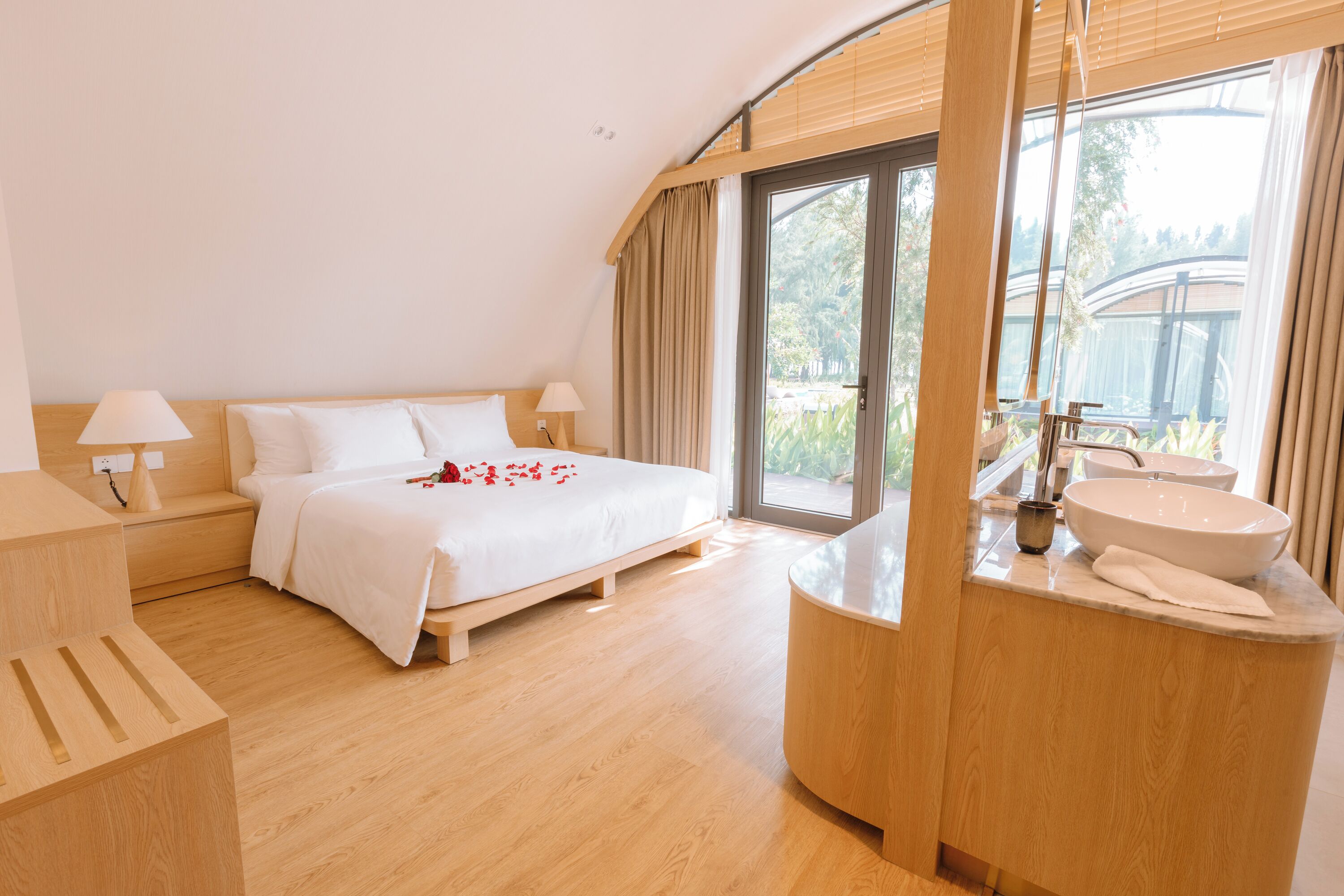 Habitació d'hotel moderna amb un llit gran, un penjador integrat amb un rentanet i una porta corredissa de vidre que dona a un balcó.