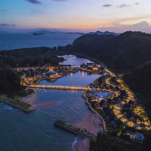 A resort with a marina, connected by a bridge, surrounded by water and hills.