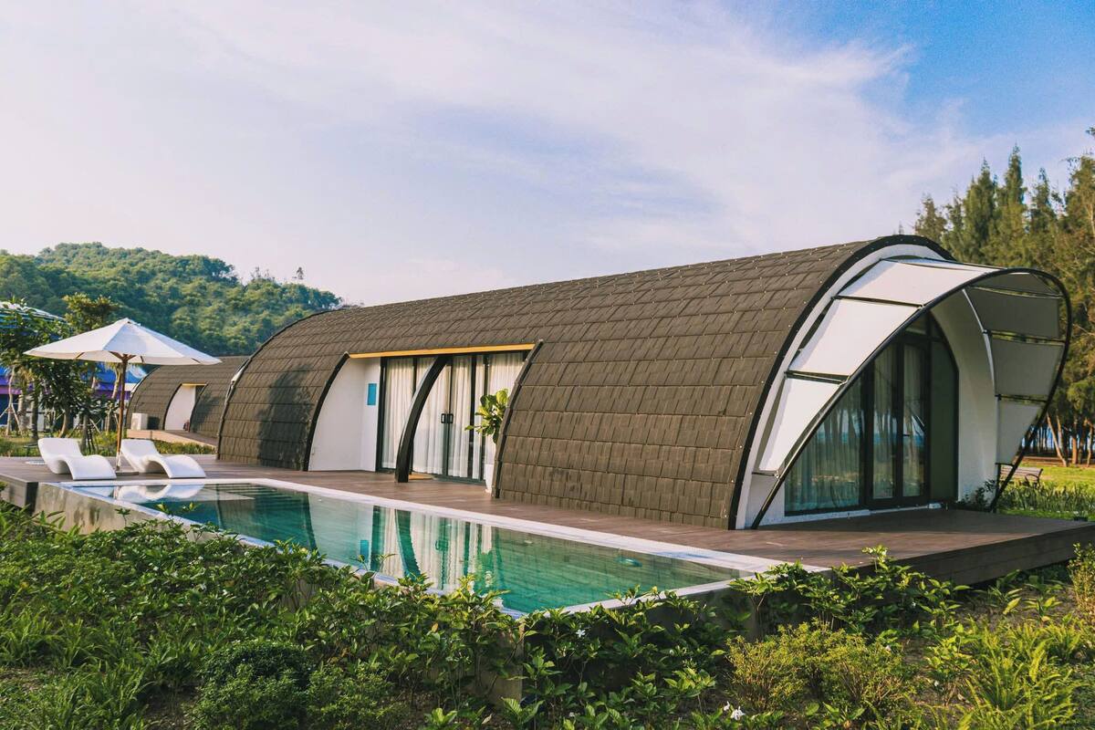 A modern building with a curved roof and large windows, adjacent to a swimming pool.