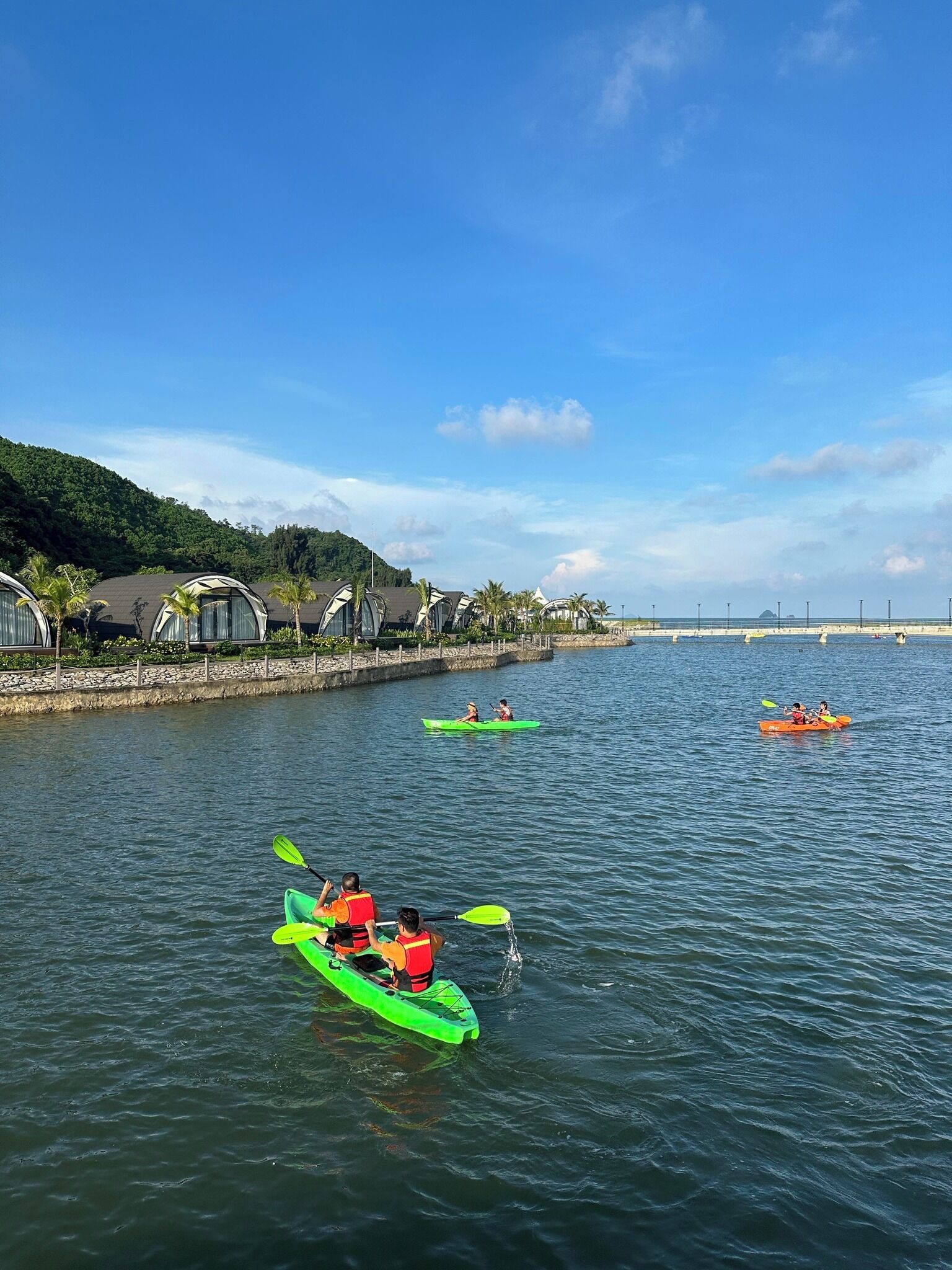 Un río tranquilo con kayaks, un puente a lo lejos y una hilera de casas a lo largo de la orilla.