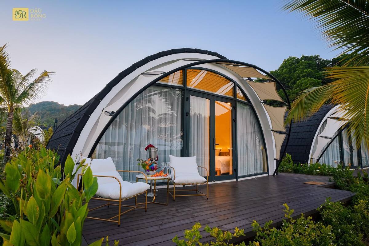 A modern, dome-shaped building with large glass windows, a wooden deck, and white furniture.