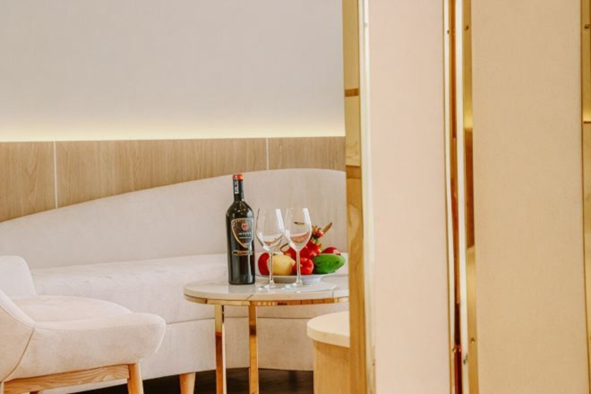A modern room with a sofa, a small round table with a bottle, glasses, and fruit.