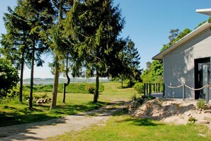 Ein Haus mit Holzfassade, ein Kiesweg, der zum Eingang führt, und im Hintergrund ein See und Hügel.
