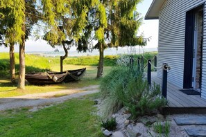 Ein Haus mit einer Holzdiele, ein Boot, das an einem Baum festgemacht ist, und eine Rasenfläche mit Blick aufs Wasser.