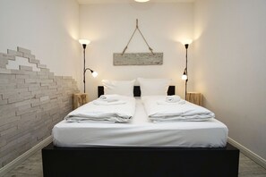 Ein Doppelbett mit weißen Leinen und Handtüchern, zwei Nachttische mit Lampen, eine Wand mit Ziegeln als Blickfang und ein rustikales Holz-Kopfteil.