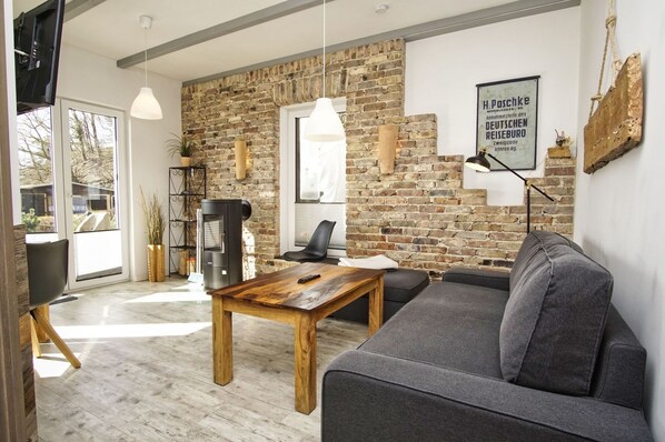 A modern living room with a brick wall, a fireplace, a sofa, and a wooden table.