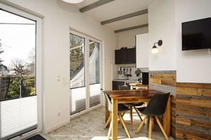 Et moderne køkken med et træbord og stole, et fjernsyn monteret på væggen, og en skydedør af glas, der fører ud til en balkon.