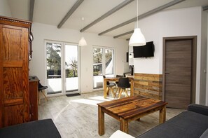 Ein geräumiges Zimmer mit einem Holztisch, zwei Stühlen, einer Couch und einem an der Wand befestigten Fernseher.