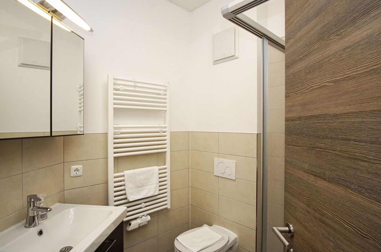 Ein modernes Badezimmer mit einem weißen Waschbecken, einem Handtuchhalter, einer Toilette und einer Duschkabine aus Glas.