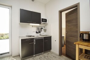 Une cuisine de taille réduite, avec des meubles de couleur sombre, un four à micro-ondes et un évier.