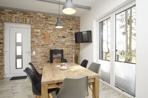 Un comedor con pared de ladrillo, chimenea, televisor montado en la pared y un ventanal con vistas a árboles.