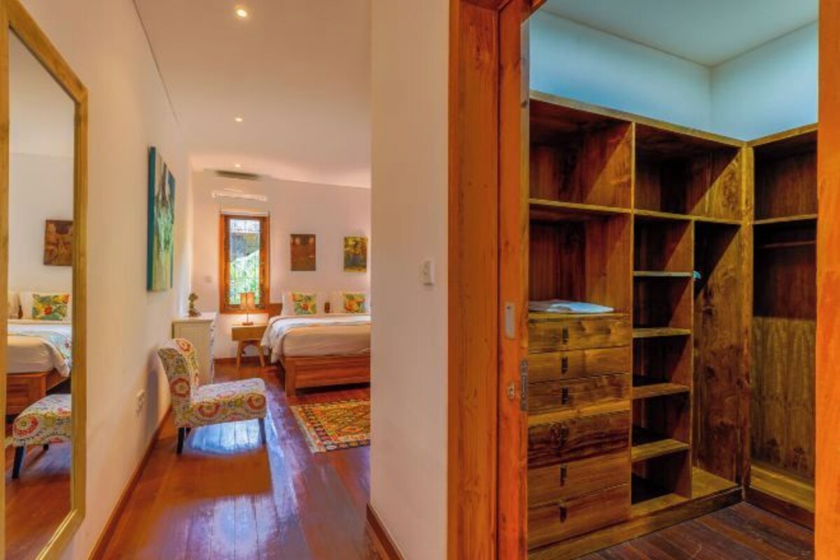 A bedroom with a wooden wardrobe, a bed, a chair, and a mirror.
