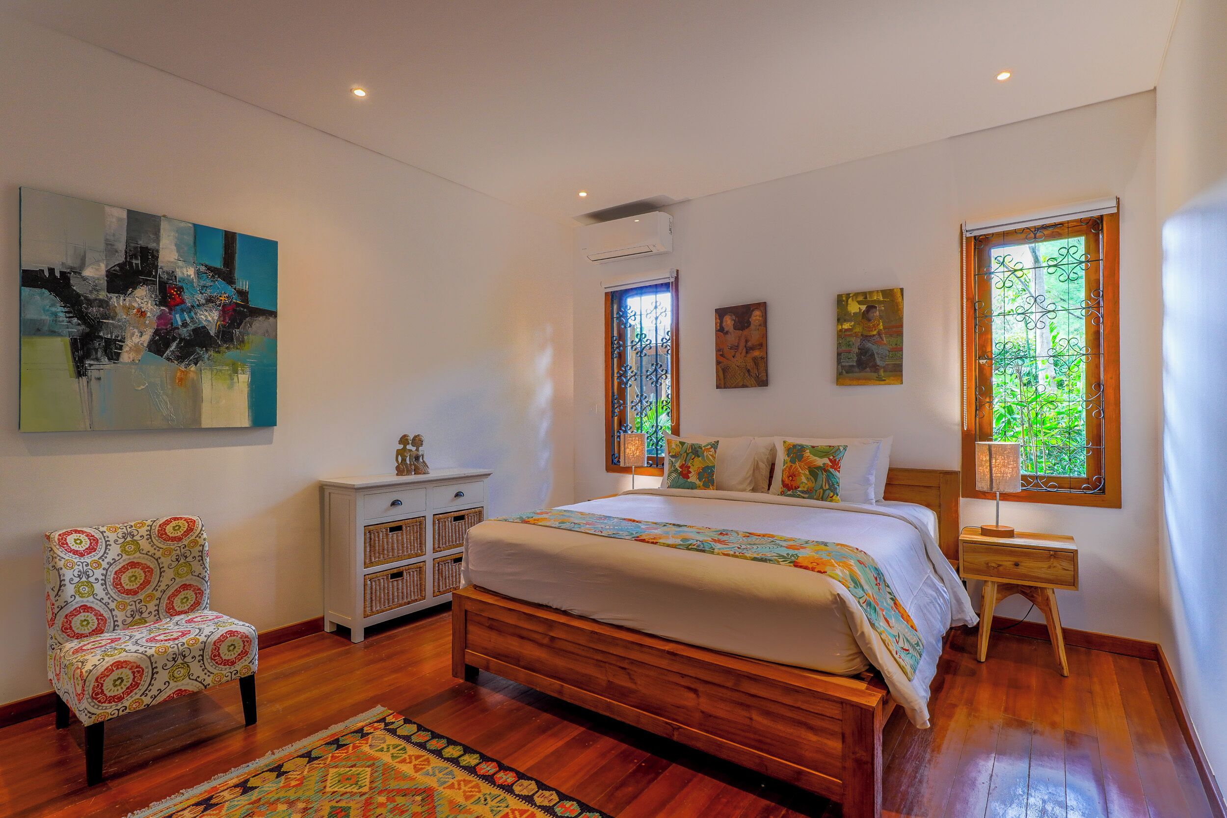 A bedroom with a wooden bed, a patterned armchair, a nightstand, and artwork on the walls.