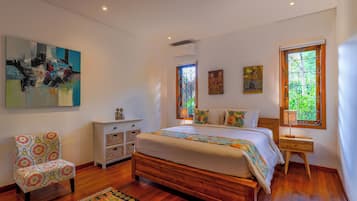 A bedroom with a wooden bed, a patterned armchair, a nightstand, and artwork on the walls.