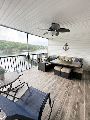 A balcony with a view of a lake, a ceiling fan, and a seating area with cushions and a table.