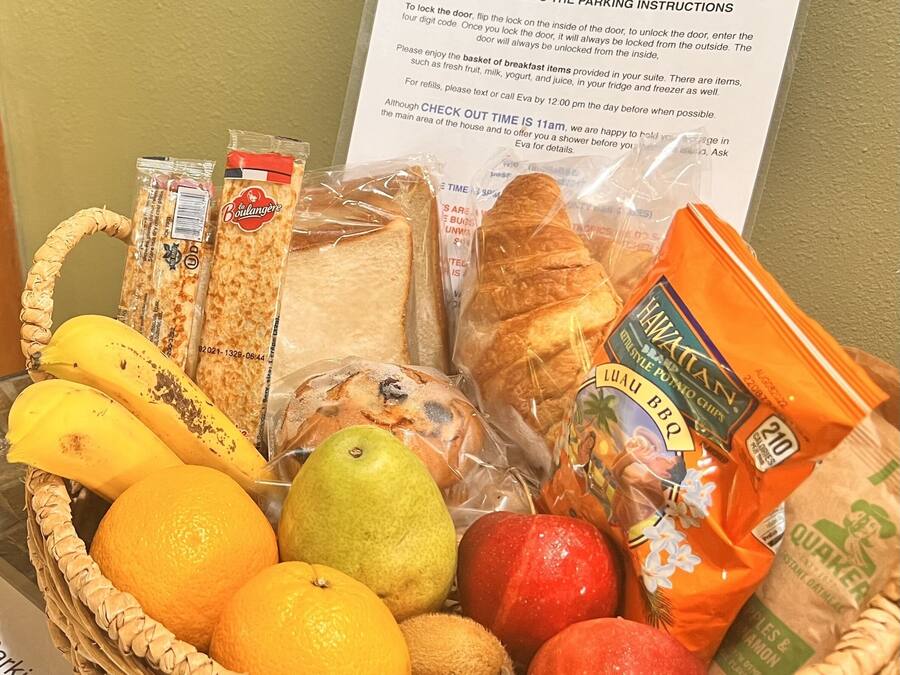 A wicker basket filled with bread, fruits, and packaged snacks, with a notice about a no check-in policy and contactless check-in instructions.