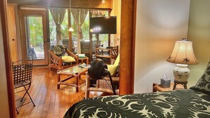 Una habitación con una cama, televisión, mesa, sillas y ventilador.