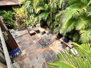 Un patio con mobiliario exterior, suelo de baldosas y abundante vegetación.