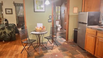 A compact kitchen with a refrigerator, a dining table with chairs, and a small window with curtains.