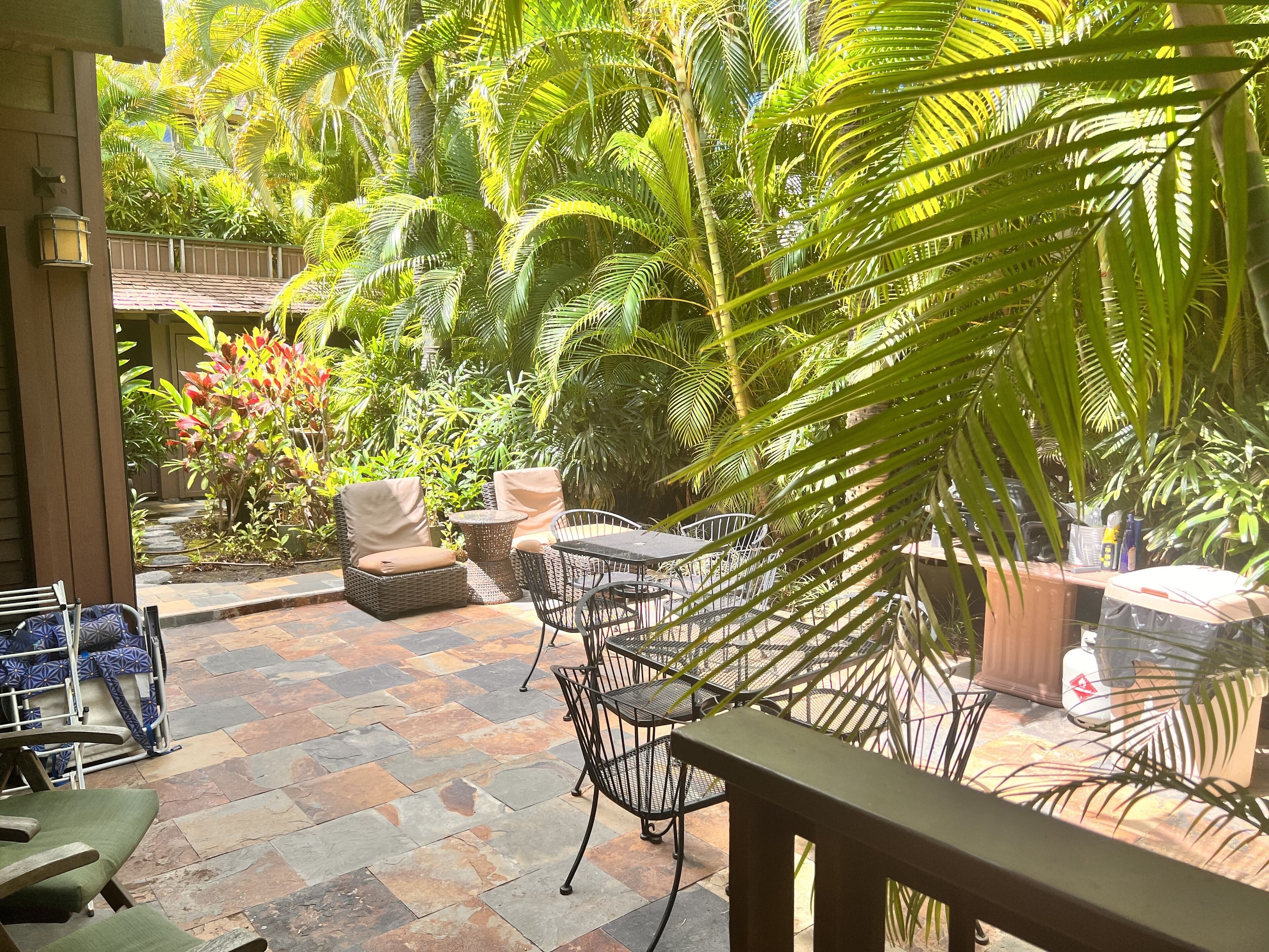 A patio area with stone flooring, wicker furniture, and lush greenery.
