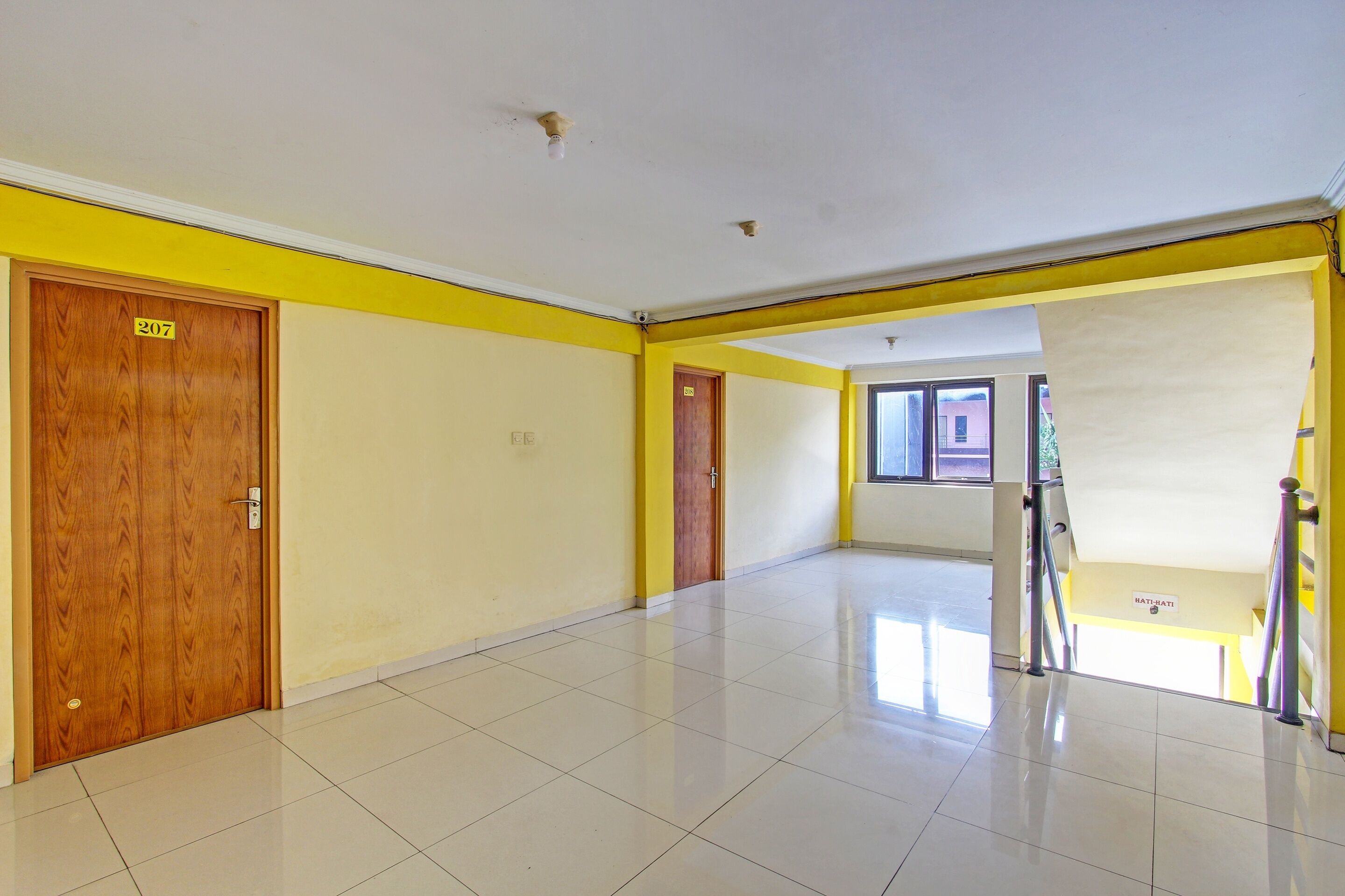 A spacious, well-lit hallway with a tiled floor, wooden doors, and a yellow accent wall.