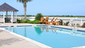 A swimming pool with lounge chairs, a gazebo, and a white fence.