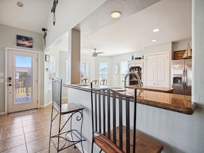 A modern kitchen with a central island, stainless steel appliances, and a dining area with bar stools. - Vitamin Sea Retreat by Ryson Vacation Rentals (Galveston)