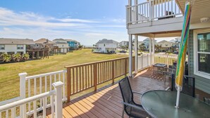 A deck with a table and chairs, a white railing, and a view of neighboring houses. - Vitamin Sea Retreat by Ryson Vacation Rentals (Galveston)