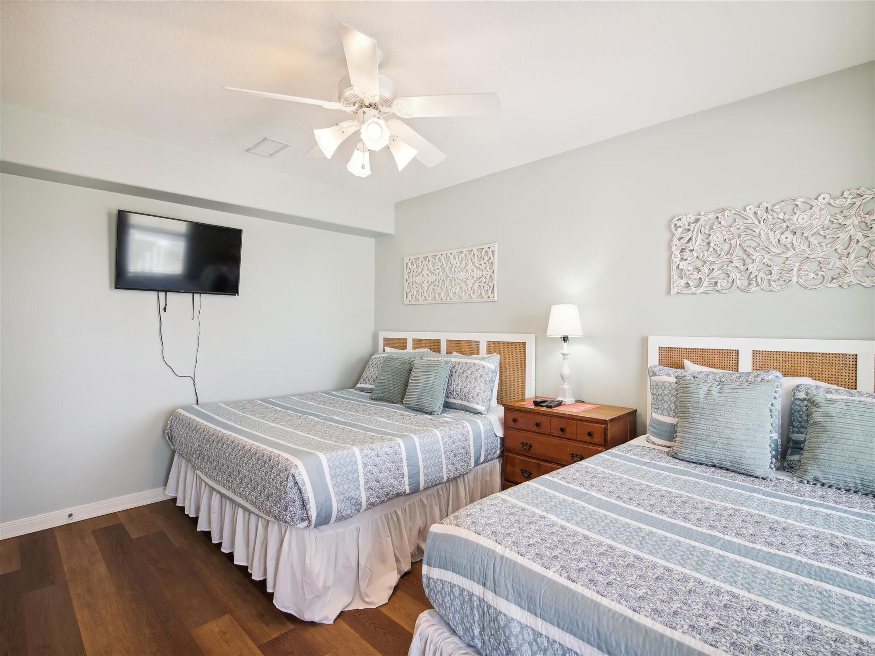 A bedroom with two beds, a ceiling fan, a TV, and decorative wall art.