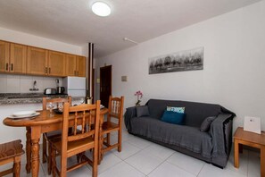 Un espace de vie compact comprenant un coin repas, une kitchenette et un canapé gris.