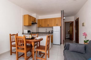 Une cuisine compacte dotée de meubles en bois, d’un four à micro-ondes, d’un réfrigérateur et d’une table à manger avec des chaises.