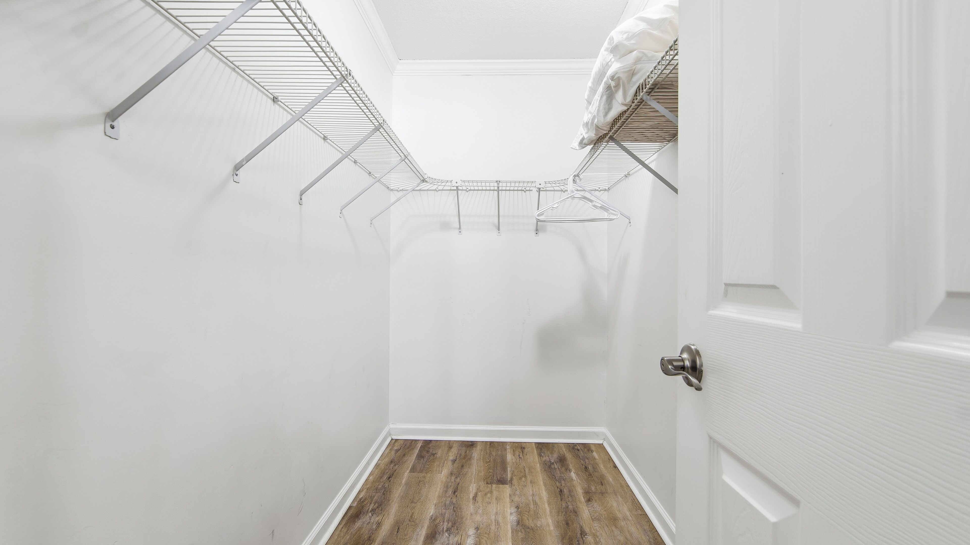 A narrow hallway with a wooden floor, white walls, and a metal rack with clothes hanging.