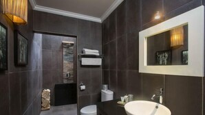 Een moderne badkamer met donkere tegels, een witte wastafel, een toilet en een handdoekrek.