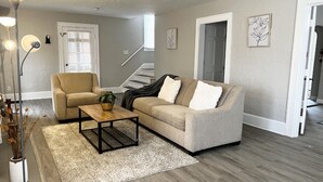 A living room with a beige sofa, a wooden coffee table, and a white rug. There is a staircase in the background leading to another room. - Stanley Cozyside (Middletown)
