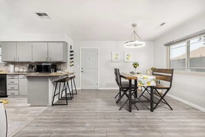 A modern kitchen with a central island, bar stools, and a dining table with chairs.
