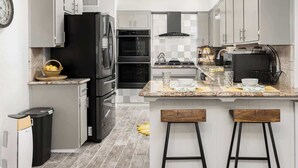 A modern kitchen with grey cabinets, a black refrigerator, a stove, and a sink. There are two stools at the island.