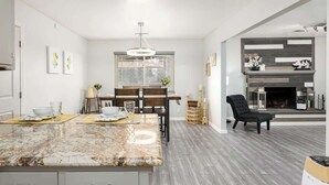 A modern kitchen with a marble island, wooden dining table, and a fireplace.