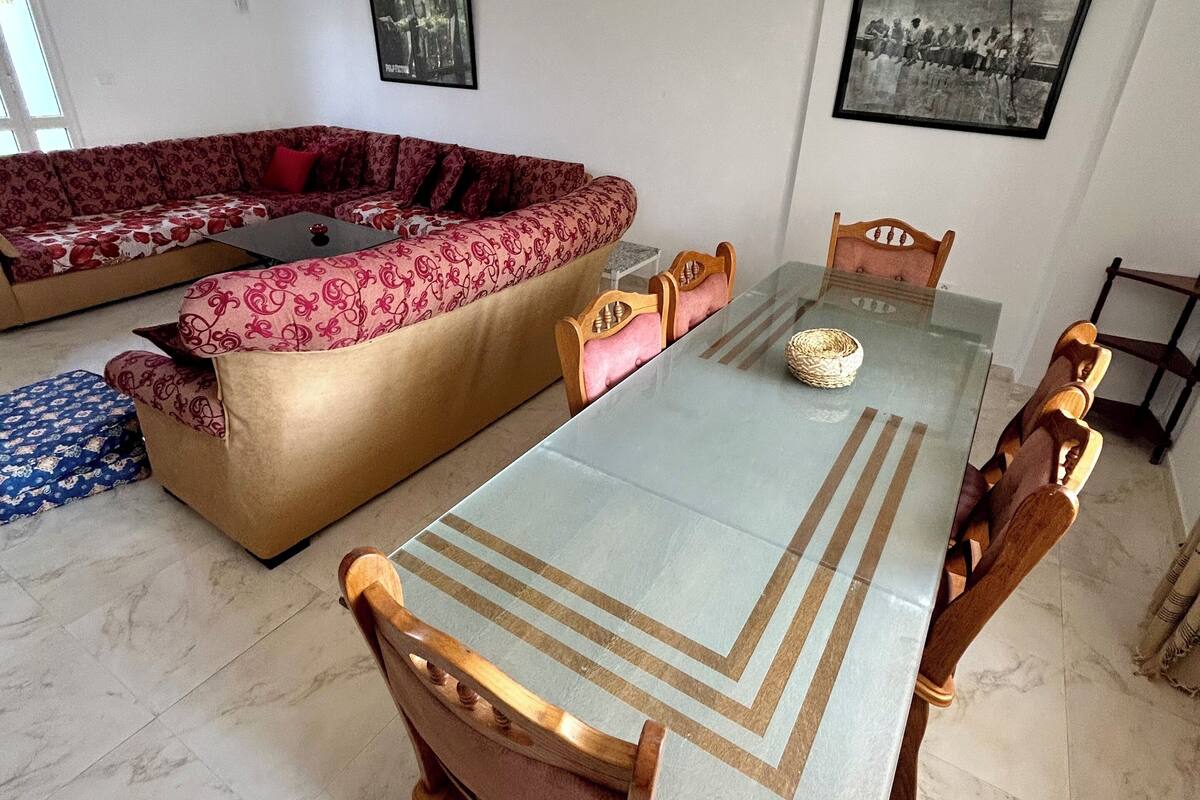 Un salon spacieux avec un grand canapé d’angle, une table à manger avec des chaises et un plafond doté d’un éclairage encastré.