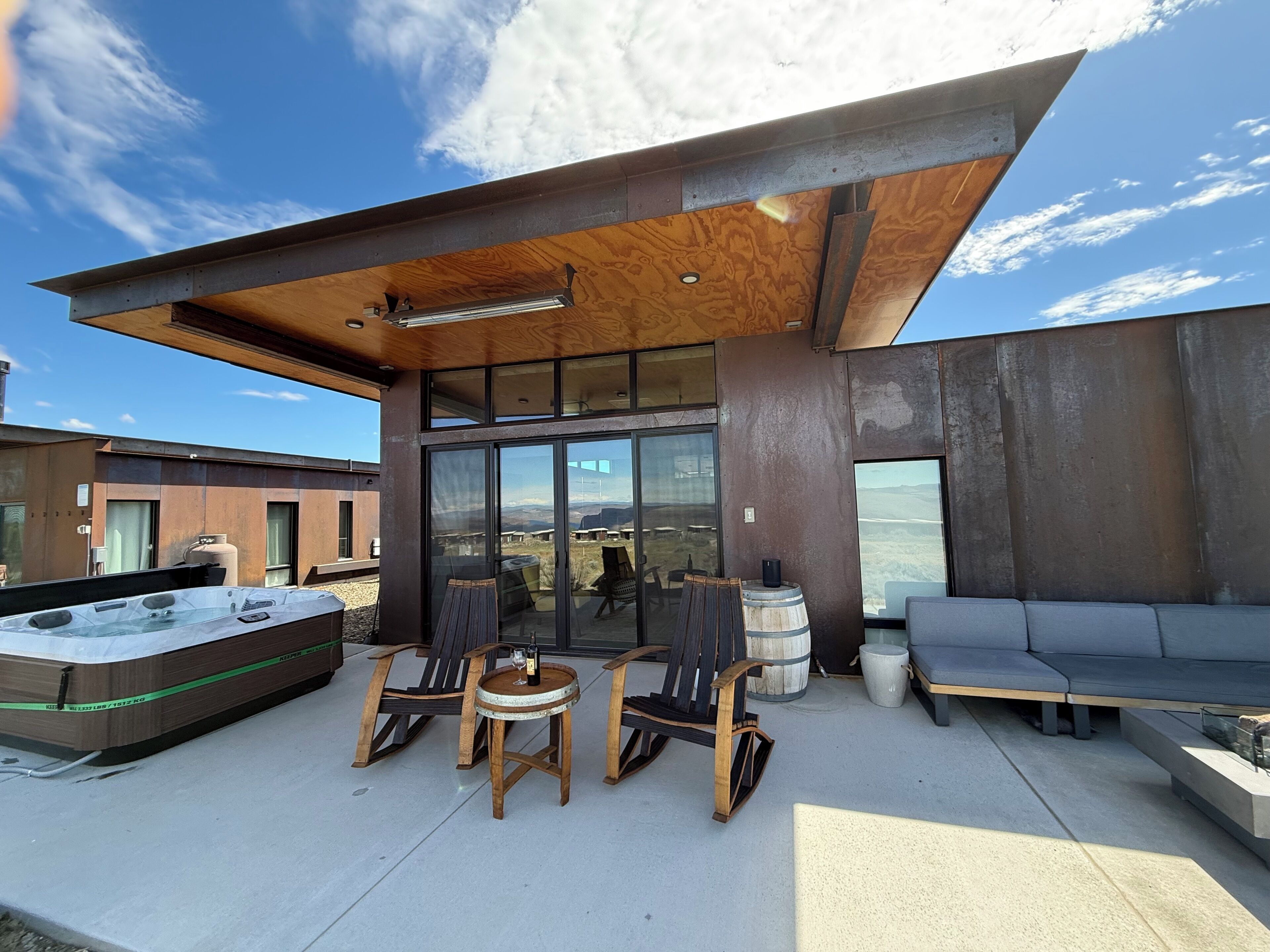A modern outdoor seating area with a hot tub, wooden chairs, and a sofa.