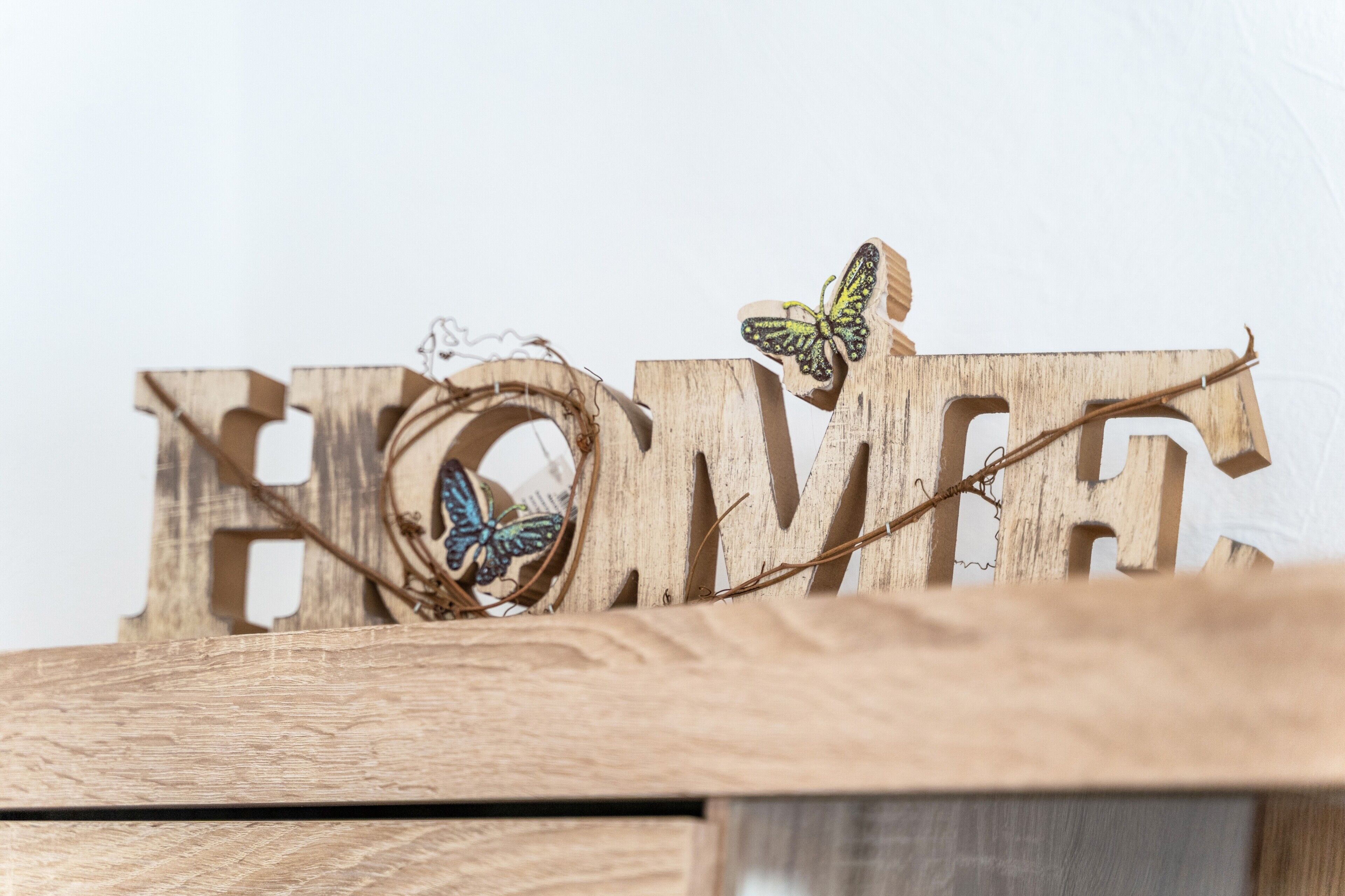 Holzbuchstaben, die das Wort 'HOME' bilden, mit einem Schmetterling auf einem der Buchstaben.
