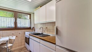 Una cocina con encimera de madera, armarios blancos, un lavamanos y una ventana con persianas.